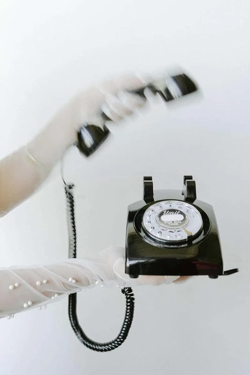 Gloved hands holding a black rotary telephone used as an audio guest book.