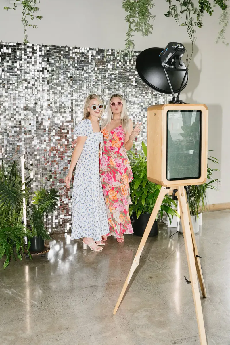 Two guests posing with sunglasses in front of a shimmer wall at the photo booth.