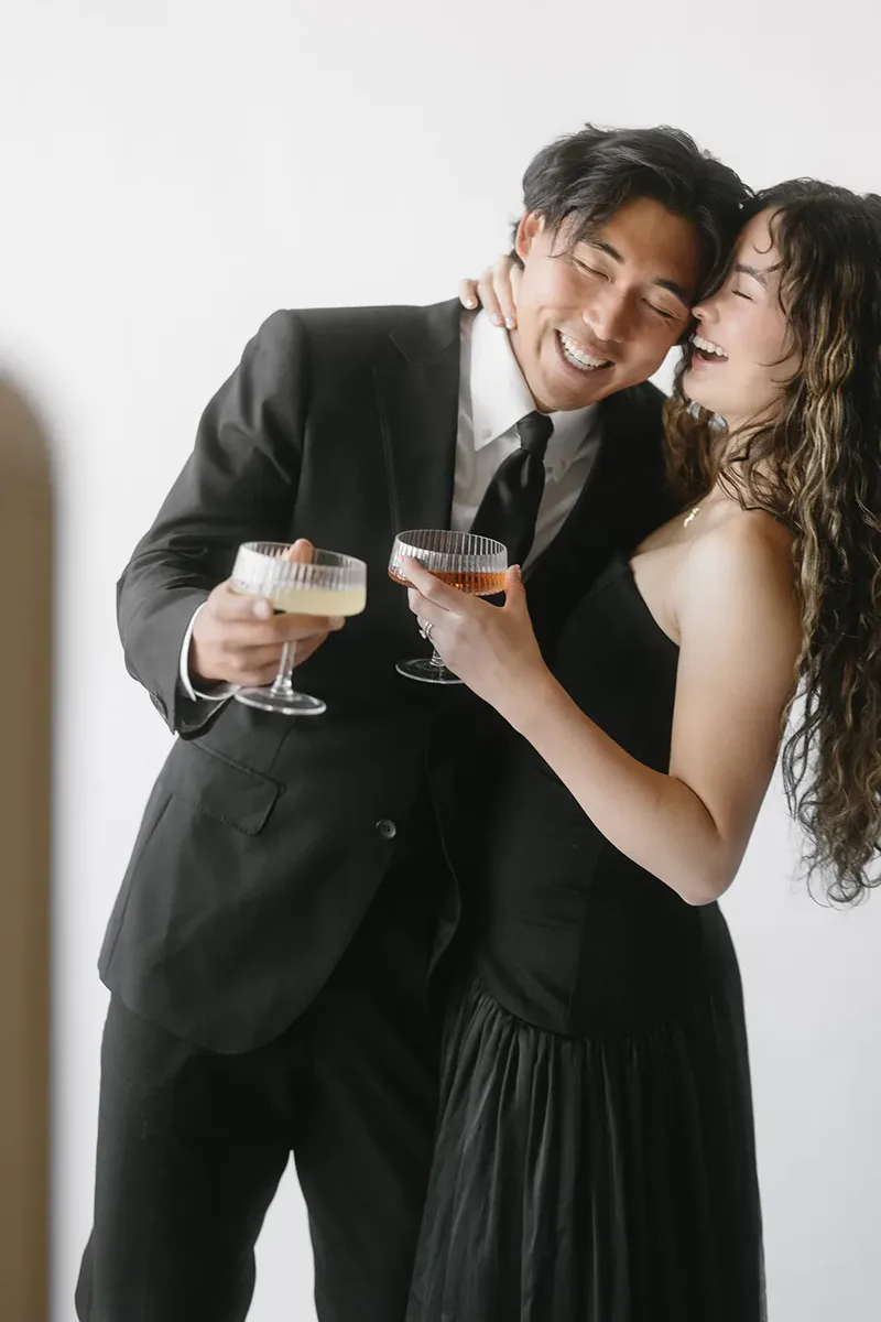 Smiling couple in formal attire toasting with coupe glasses at the photo booth.