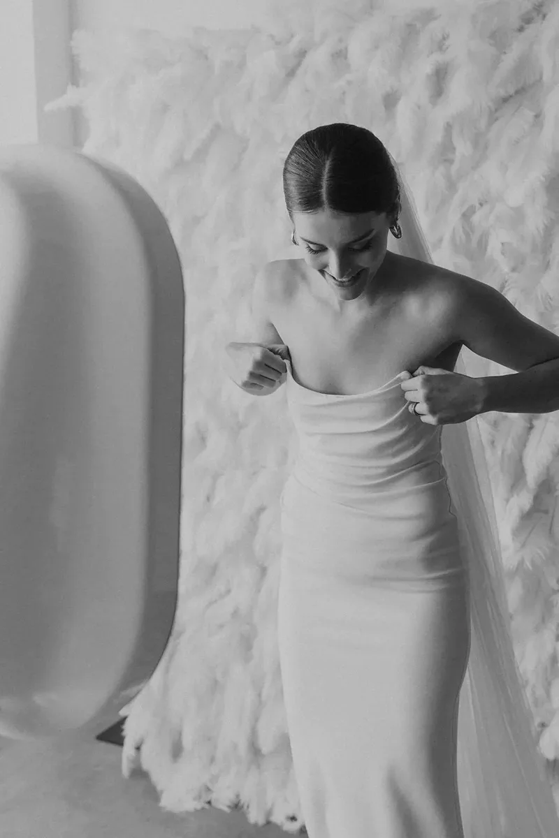 Bride posing beside the photo booth in front of a white feather wall.